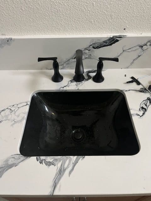 Black sink with elegant faucet set on a marble countertop featuring distinctive veining.