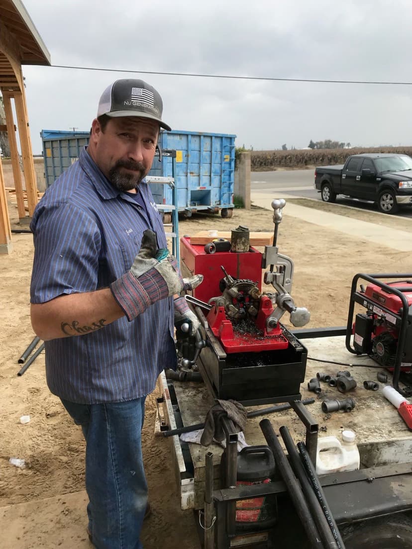 Mechanic working on machinery with tools, wearing gloves and a cap, on a construction site.