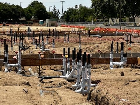 Construction site with plumbing pipes and foundations being laid for a new building project.
