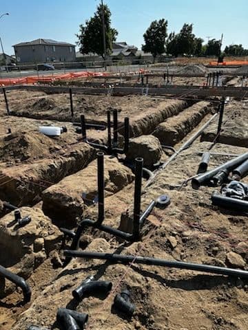Construction site with exposed pipes and foundational trenches in a residential area.