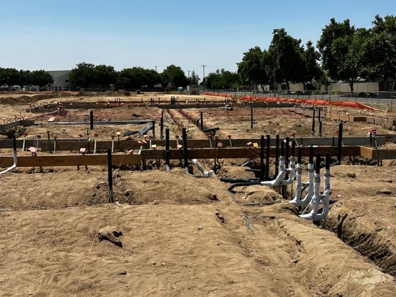 Construction site with foundation and plumbing work in progress on sandy terrain.