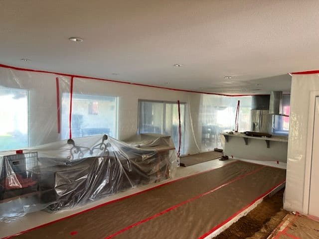 Indoor renovation scene with plastic sheeting, revealing a partially covered kitchen and living area.