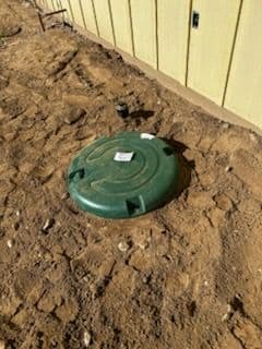 Green septic tank lid installed in dirt near a house foundation.