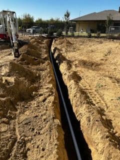 Excavated trench with PVC pipe installation at a construction site.
