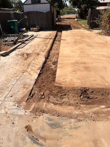 Dirt pathway under construction alongside a residential fence and storage shed.