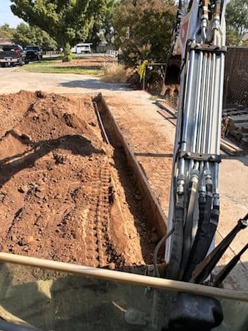 Excavator preparing a trench for construction in a dirt-filled area.
