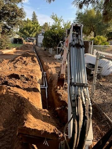 Excavator digging trench for utility installation in a residential yard.