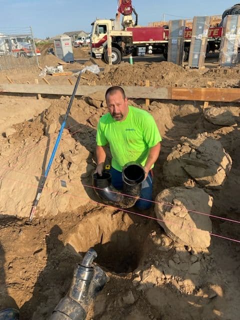 Construction worker installing plumbing pipe in a trench at a building site.