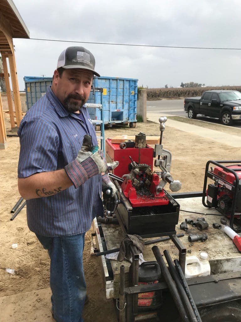 Man operating a hydraulic machine outdoors, wearing gloves and a cap, construction site background.