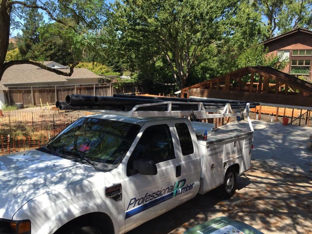 Professional plumber truck parked near a home construction site with pipes on the roof.