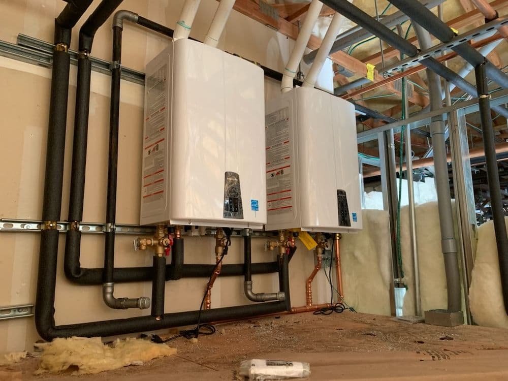 Tankless water heaters installed on a wall with copper and PVC piping in a basement.