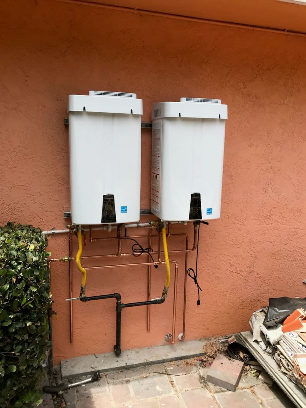Tankless water heaters mounted on a wall with plumbing connections in a residential setting.