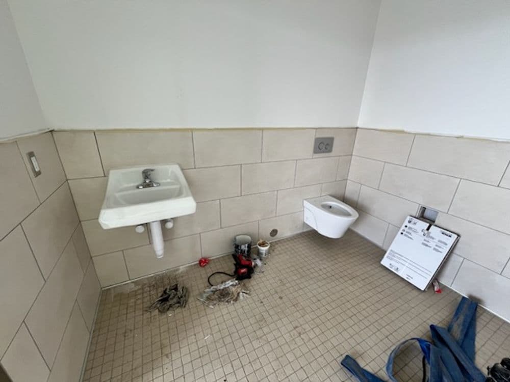 Renovated restroom with sink and toilet, featuring unfinished tiles and construction materials.