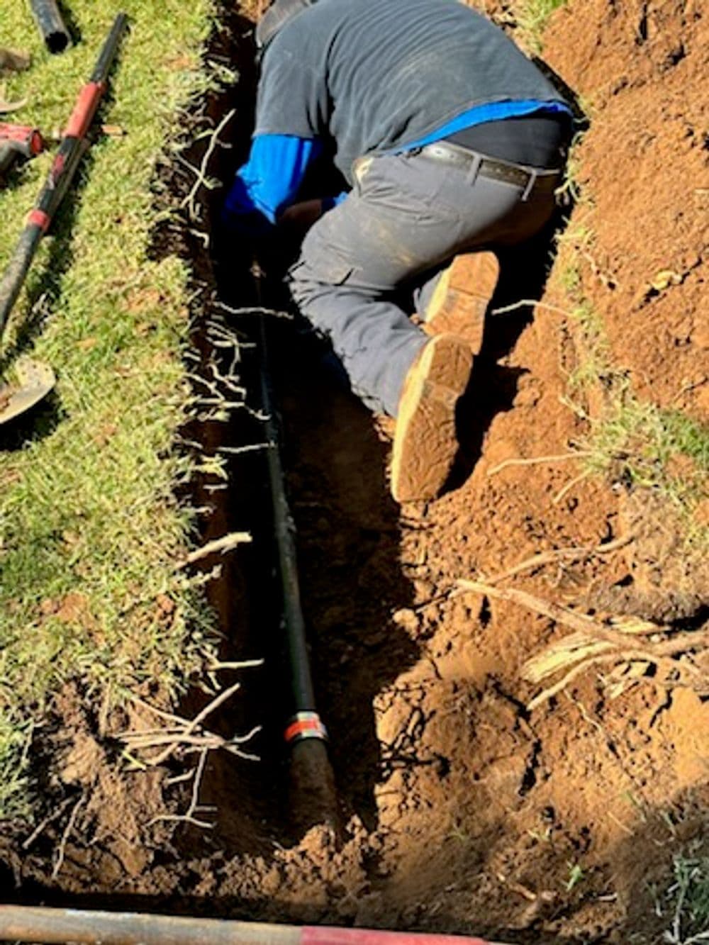 Worker installing a pipeline in a trench with tools nearby on a sunny day.