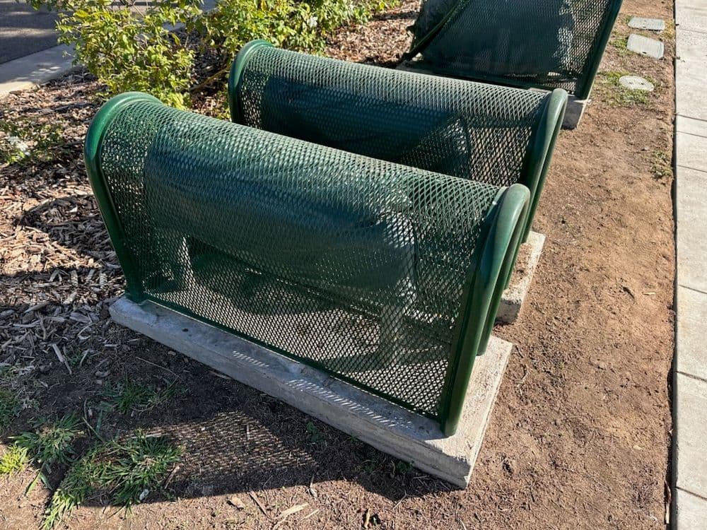 Two green mesh recycling bins placed on a path surrounded by mulch and grass.