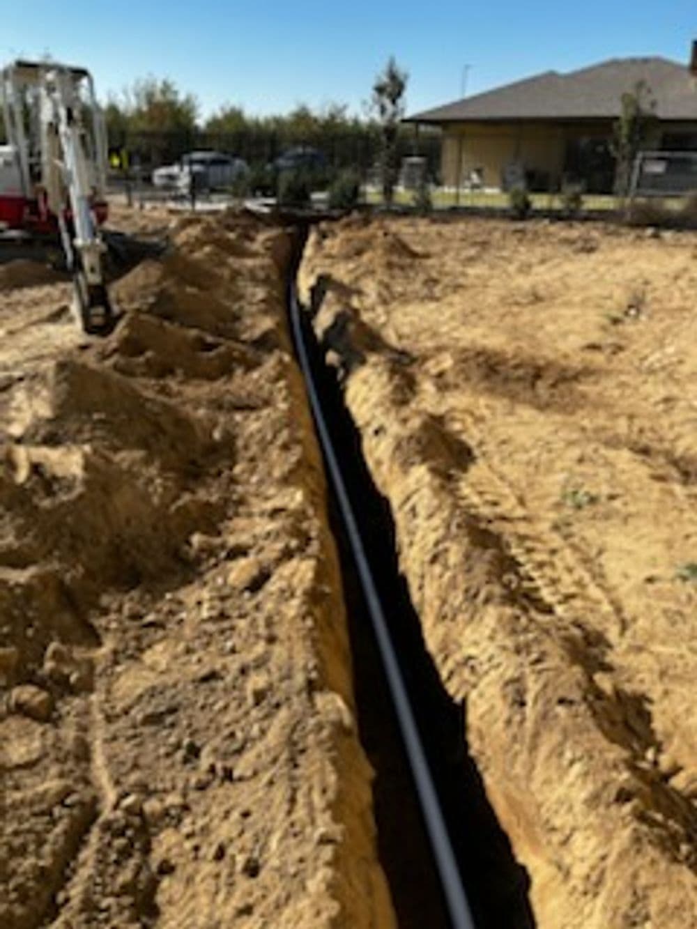 Excavated trench for utilities installation in sandy soil near residential home.