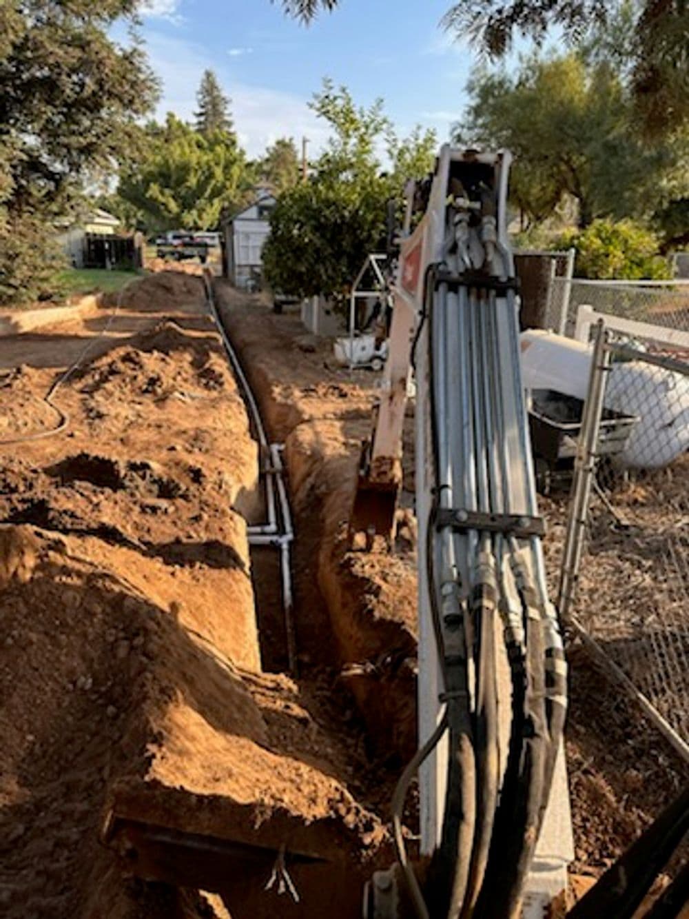 Excavator digging a trench for utility installation in a residential area.