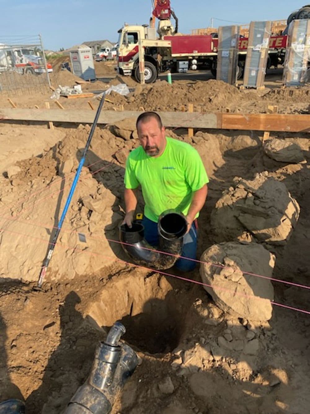 Construction worker installing pipes at a job site with machinery in the background.