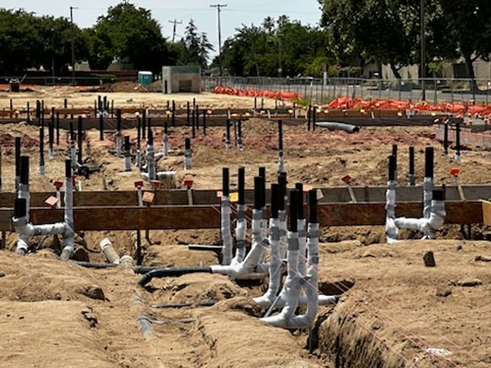 Construction site showcasing plumbing installation with pipes and foundations.