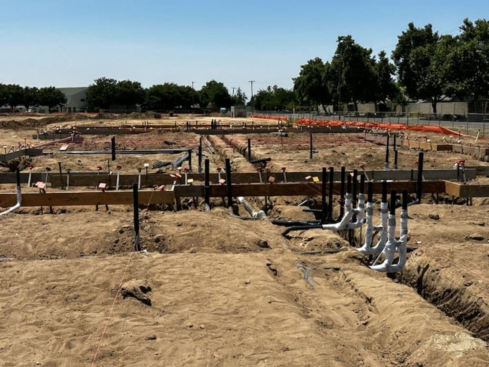 Construction site with foundation framework and plumbing installations on sandy terrain.